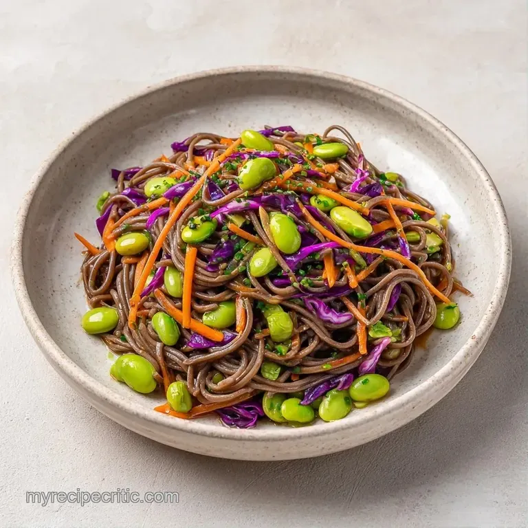 Twirled buckwheat noodles in a white ceramic bowl topped with vibrant green edamame and toasted sesame seeds.